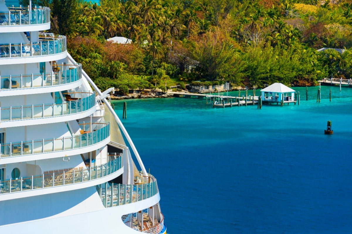 Side of a cruise ship with trees and ocean in background